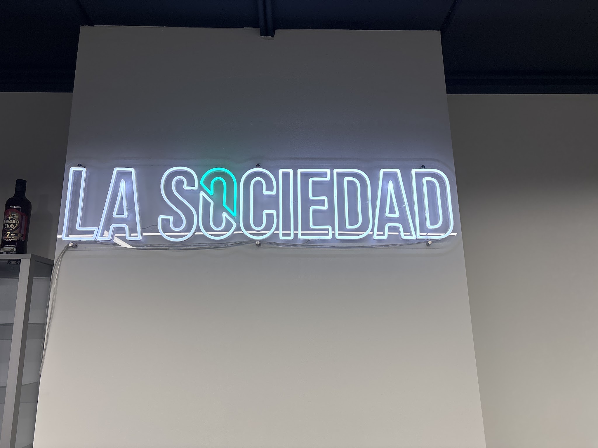 Het witte neonbord LA SOCIEDAD aan de muur, met de O in turquoise